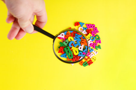 colored letters of the alphabet with a magnifying glass on a yellow background close-upの写真素材