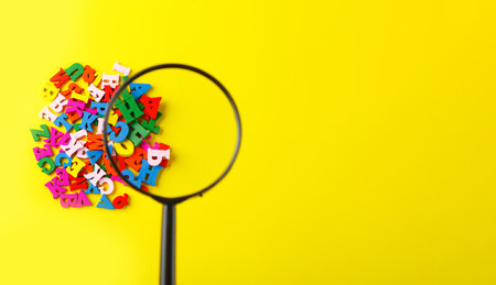 colored letters of the alphabet with a magnifying glass on a yellow background close-upの写真素材