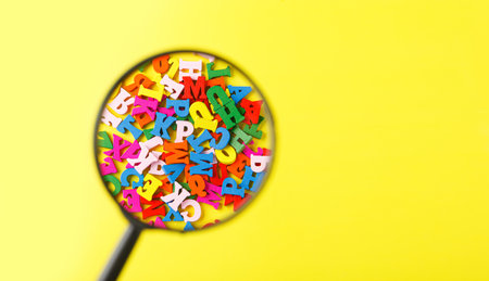 colored letters of the alphabet with a magnifying glass on a yellow background close-up