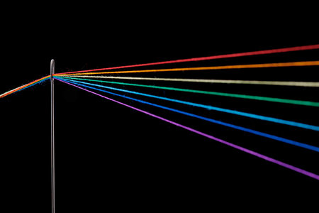 multi-colored threads for sewing in the form of a rainbow pass through an antique needle on a black...