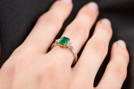 Beautiful female hand with gold ring with diamonds and emerald on gray background close-upの写真素材