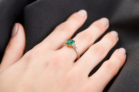 Beautiful female hand with gold ring with diamonds and emerald on gray background close-upの写真素材