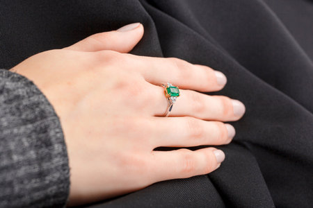 Beautiful female hand with gold ring with diamonds and emerald on gray background close-upの写真素材