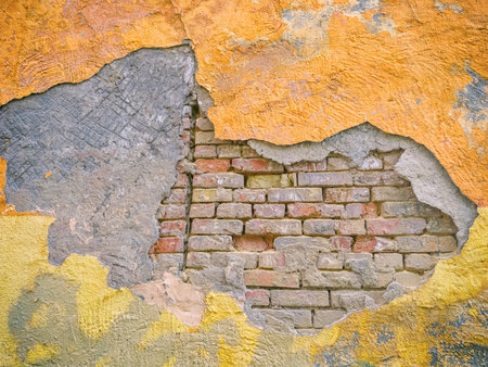 An old brick wall with peeling plaster and paint layers inspires creative design. Its rustic texture brings a unique aesthetic appeal.の写真素材