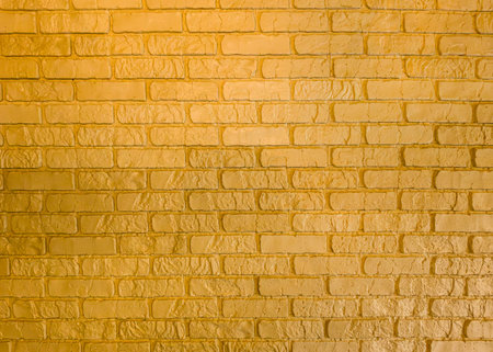 A yellow brick wall with texture in soft lighting adds warm charm. Its versatile design suits various creative projects.の写真素材