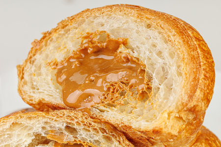 Detailed shot of a buttery croissant cut in half, showing rich caramel texture inside. Isolated on white. Great for food blogging, recipe books, and social media marketing for cafes.の写真素材