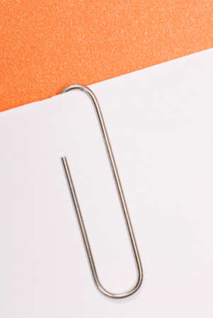 paper clip fastened to white paper with orange backgroundの写真素材