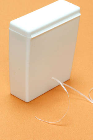 waxed dental floss in an unmarked container on an orange backgroundの写真素材