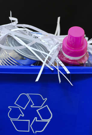 a blue recycling bin full of recyclable things - bottles, shredded paper and tin cans