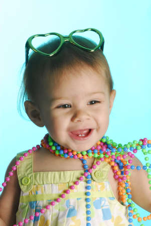 cute baby wearing colorful beads and heart shaped sunglasses on blue backgroundの写真素材