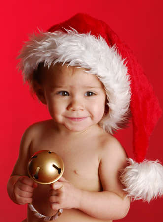 baby wearing santa hat holding christmas decoration on red backgroundの写真素材
