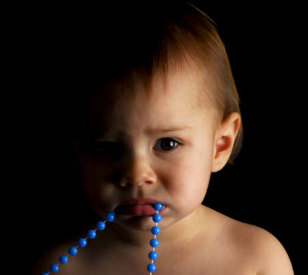 baby girl with blue beads in mouth on black backgroundの写真素材
