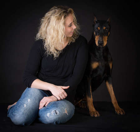 woman sitting beside doberman pinscher on black backgroundの写真素材