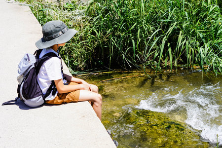 ten year old boy sitting on a bridge over a river on a nature hikeの写真素材