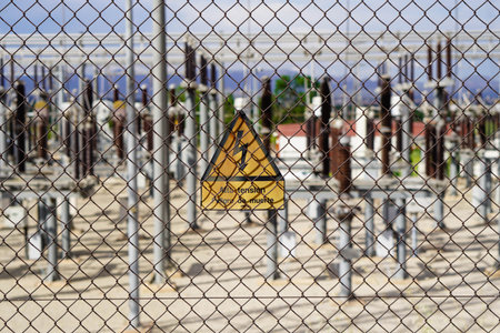 A yellow sign with a black border is on a fence. The sign warns of danger high voltage, danger of...