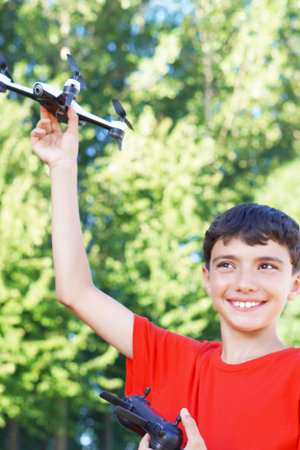 smiling tween boy playing, ready to fly drone in the field in summertime