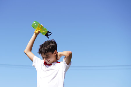 boy in sports gear pouring water over himself to cool offの写真素材