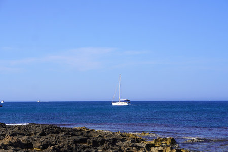 summer sea scene from a rocky beach with sea and blue sky and a ship on the horizonの写真素材