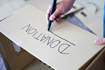 Hands writing the word "donation" on a cardboard box, preparing items to give away while moving house.の写真素材