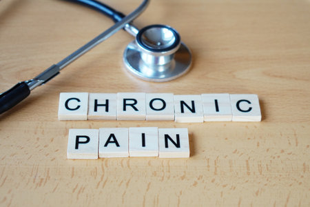 Medical concept image representing chronic pain. Wooden letters spelling "chronic pain" arranged on a light surface with a stethoscope placed beside them. Symbolic composition emphasizing long-term health conditions and pain management. Suitable for healthcare, diagnosis, and wellness-related topics.の写真素材