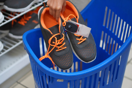 Teenage boy selecting sneakers and placing them in a shopping cart at mall during sales and...