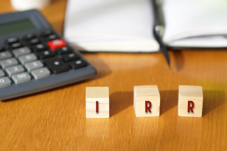 IRR, financial concepts. Letters written on wooden blocks with a calculator and notebook in the backgroundの写真素材