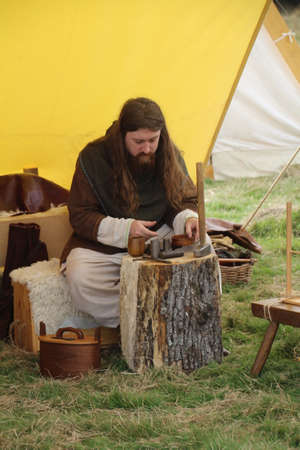 Battle, UK - 14 October, 2018: Man in saxon period clothing demonstrating how to make hammered coinage at a Battle of Hastings reenactment weekend.のeditorial素材