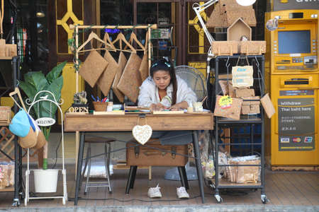 Phuket, Thailand - 28 November, 2018: Young Thai woman making purses out of cork outside of the front of her shop.のeditorial素材