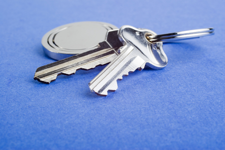 Set of silver coloured house keys on blue texture background. Shallow DOF, focus on end of second key. These are used house keys with a few scratches. Lots of copy space.の写真素材