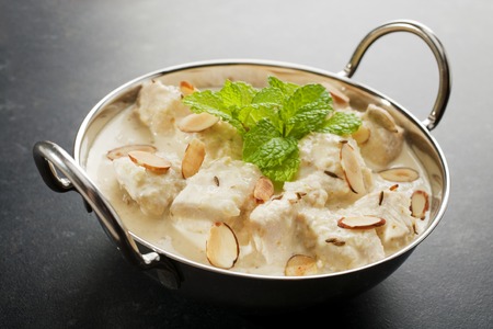Mild and Creamy chicken korma, in a balti dish, garnished with mint, almonds and toasted cumin seeds, on a dark background.の写真素材
