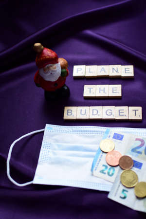 A medical mask, coins and a Christmas elf on a purple background. The concept of Christmas and New Year.の写真素材