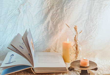 A stack of books, a burning candle and a bouquet of dried flowers on a light backgroundの写真素材