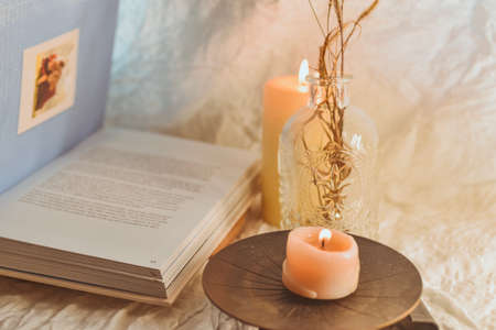 Burning candle in a glass vase on a wooden stand next to an open book on a light backgroundの写真素材