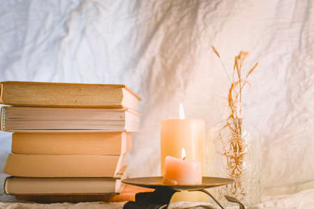A stack of books and a burning candle on a glass stand.の写真素材