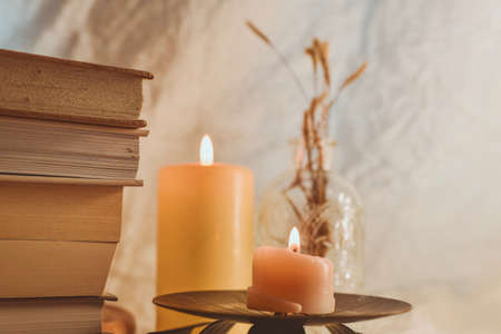 A stack of books, candles and dried flowers on a wooden stand on a light background.の写真素材