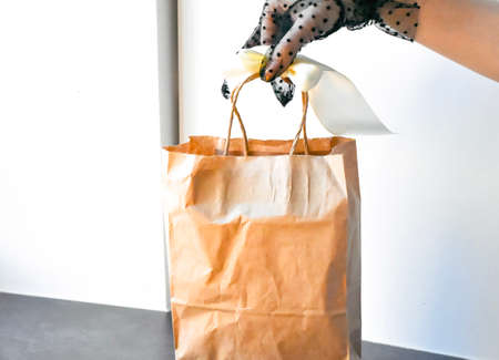 Woman hand in black gloves holding paper bag with food. Food delivery concept.の写真素材