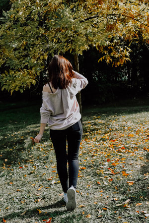 A young girl in a white T-shirt and black jeans walks through the autumn park.の写真素材