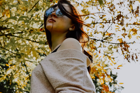Portrait of a beautiful young brunette girl in a coat and sunglasses on the background of autumn leaves.の写真素材