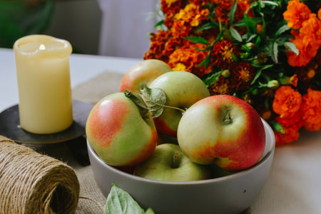 Apples in a bowl with a burning candle and a bouquet of flowers