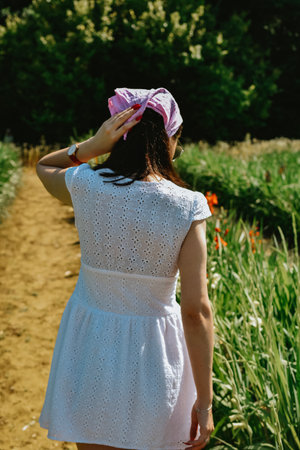 Girl in a white dress and a pink scarf on her head stands in the fieldの写真素材