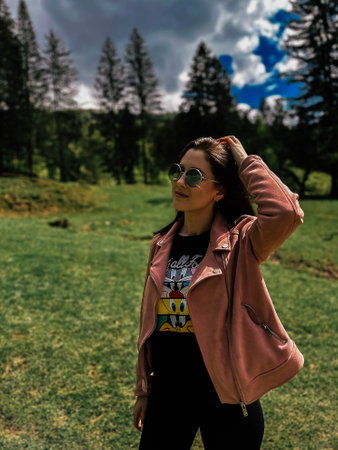 Beautiful young woman in a pink jacket and sunglasses on a green meadow