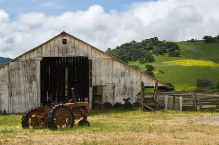 Old wooden barn with rusted tractor sitting out front.の写真素材