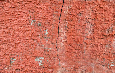 Red concrete wall with cracked paint and plaster. Suitable as a texture and as the background for the design of promotional materials.の写真素材