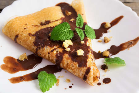 Pancake with chocolate and nuts, decorated with mint leaf Pancake with chocolate and nuts, decorated with mint leaf on a white plateの写真素材