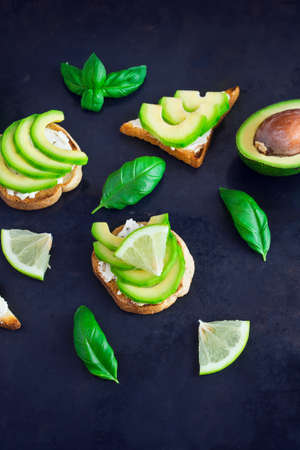Toast with avocado, cream cheese curd and lime on a dark background.