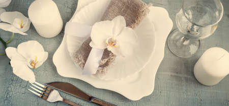 Spring table setting with orchid decorations, candles, wineglass on a gray background. Top view....