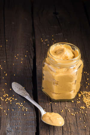 Fresh mustard sauce in a jar and mustard seeds scattered on the old wooden background.の写真素材