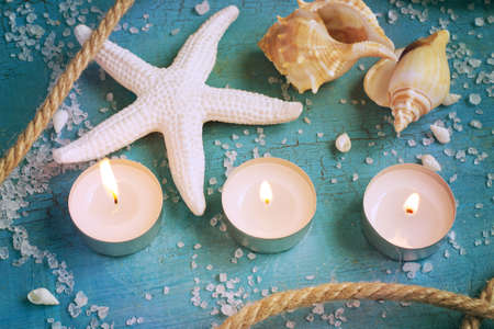 Three burning candles, starfish and shells on the turquoise vintage background. Tinted.の写真素材