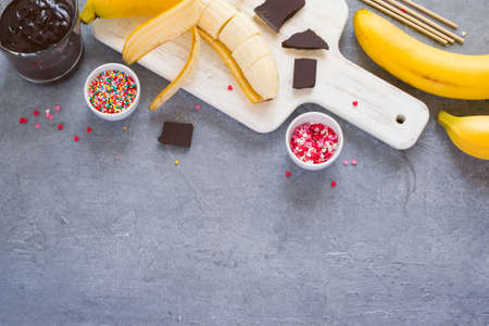 Background Cooking Banana Pops - bananas, dark chocolate, sugar sprinkling and cutting board, gray concrete background, space for texttop viewの写真素材