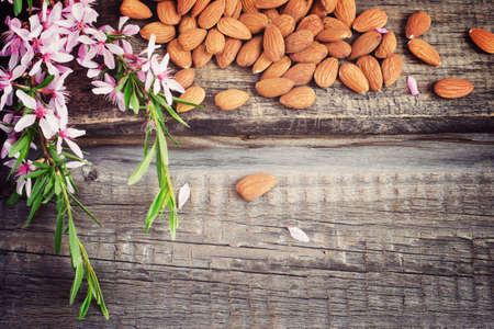 Old wooden background with crumbled almonds and flowers, tinted. Top view with copy spaceの写真素材